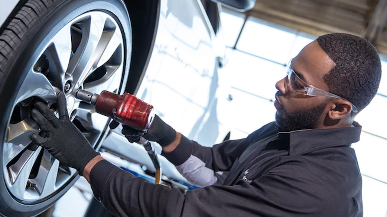 Auto service technician using an impact wrench to tighten a car's wheel.