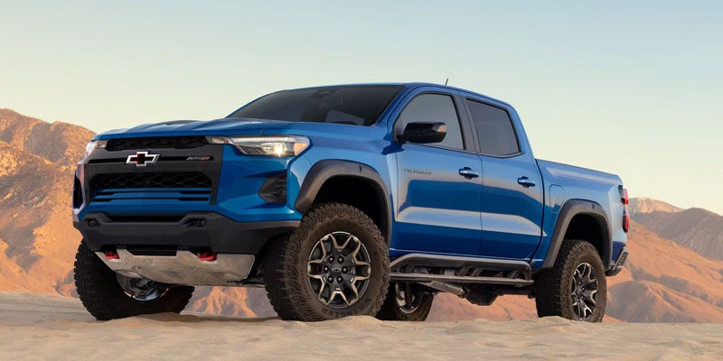 Blue Chevrolet Colorado pickup truck parked on rugged terrain with mountains in the background.
