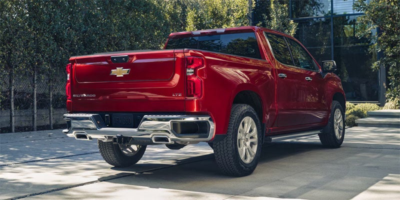 Red Chevrolet Silverado pickup truck parked on a paved driveway outside a modern building, shown from the rear three-quarter angle