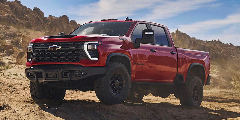 Red Chevrolet Silverado ZR2 pickup truck parked on rugged desert terrain with rocky hills in the background