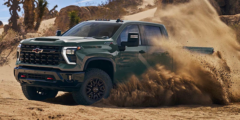 Dark green Chevrolet Silverado ZR2 pickup truck driving through deep sand in a desert landscape