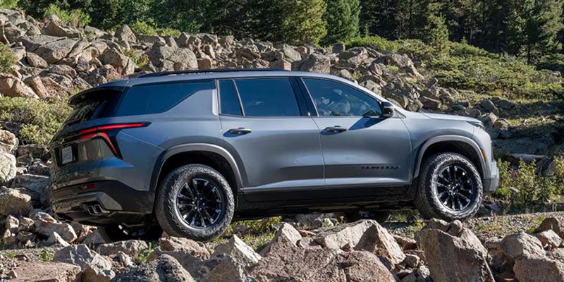 Rear three-quarter side view of a gray SUV driving over a rocky off-road trail