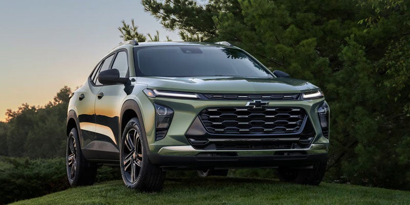 Light green Chevrolet SUV parked on a grassy area, shown from a front three-quarter angle with trees and evening sky in the background