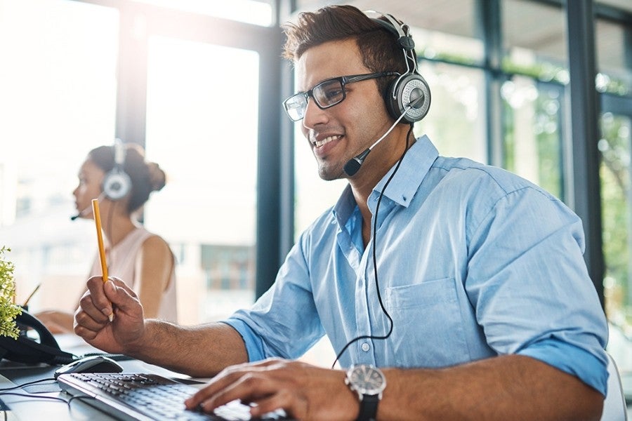 Customer service representative wearing a headset and glasses, working at a computer in a modern office environment