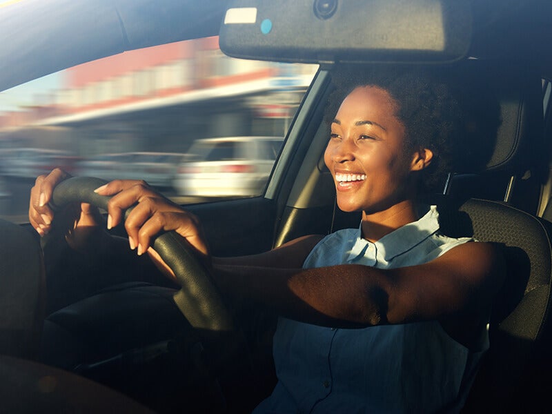 Person driving a vehicle, viewed from inside the cabin, with hands on the steering wheel