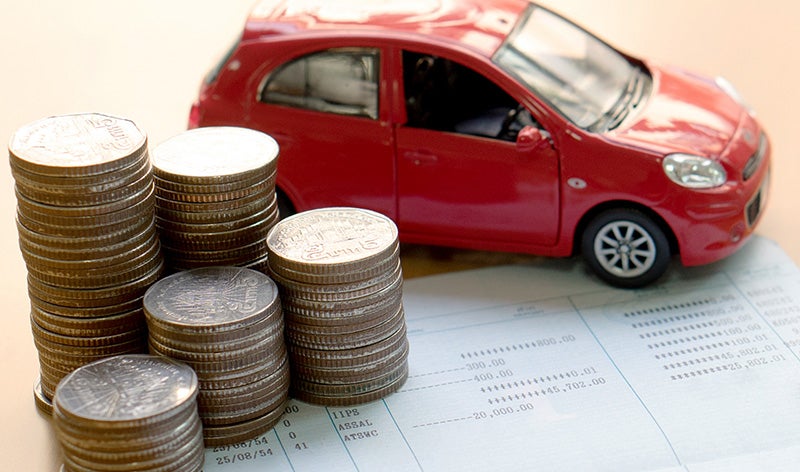 Stacks of coins placed on a financial document beside a red compact car model, illustrating car costs, financing, insurance, or vehicle savings